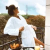 Femme sur un balcon d'hôtel 5 étoiles, vêtue d'un peignoir élégant, admirant une vue panoramique et luxueuse.