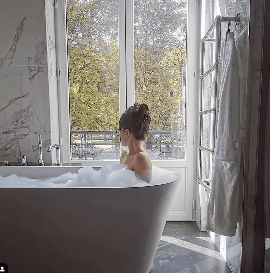 Femme prenant un bain relaxant dans une baignoire de luxe, entourée de linge de maison d'exception, alliant confort et élégance.